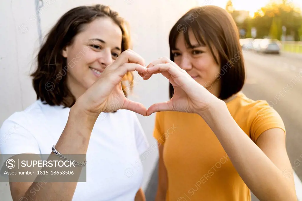 Young lesbian couple making heart with hands during sunset