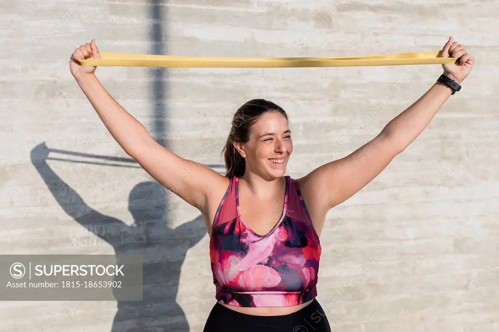 Happy female athlete stretching resistance band while exercising during sunny day