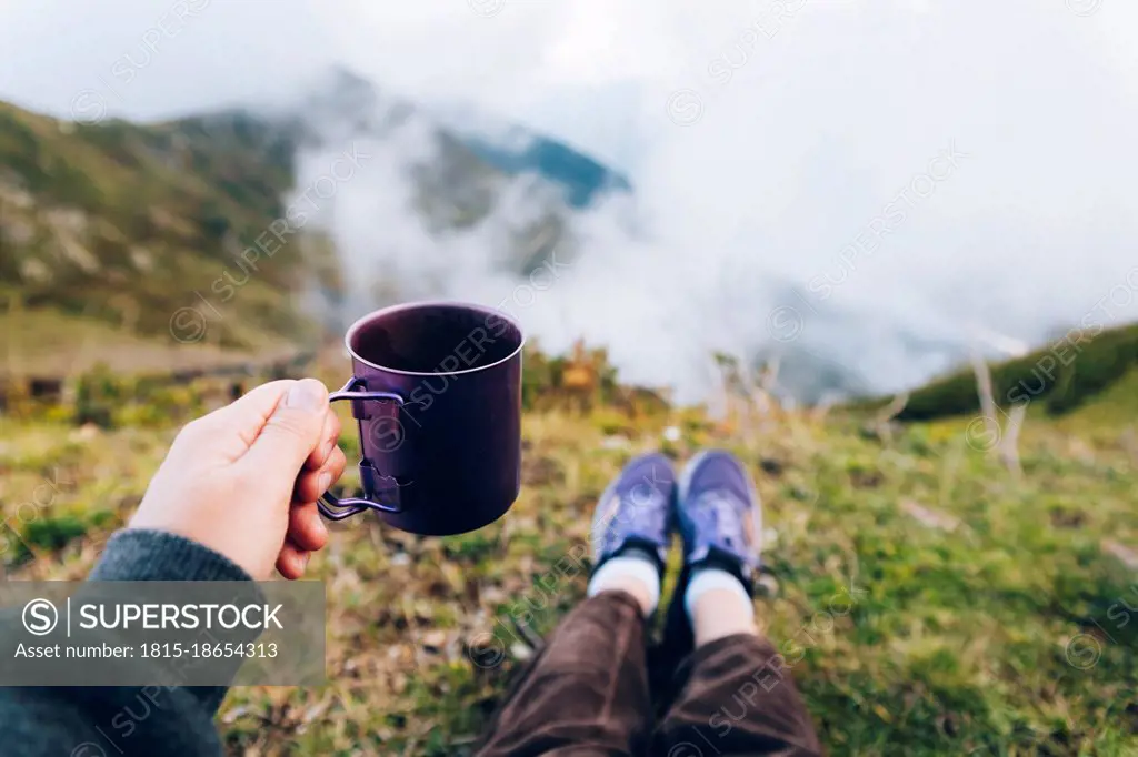 Woman holding cup of tea while sitting on mountain