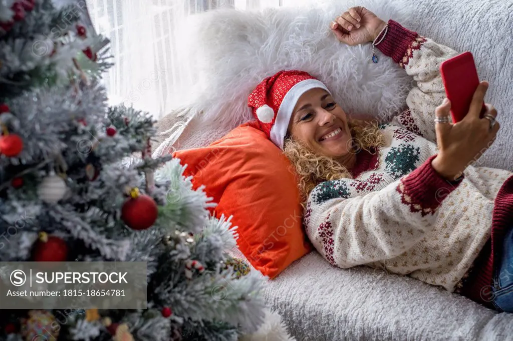 Woman wearing Santa hat taking selfie through smart phone at home