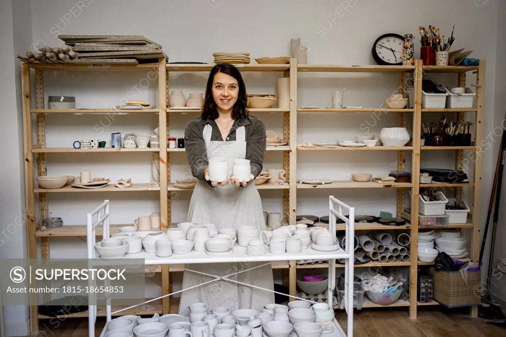 Smiling female potter showing ceramics in workshop