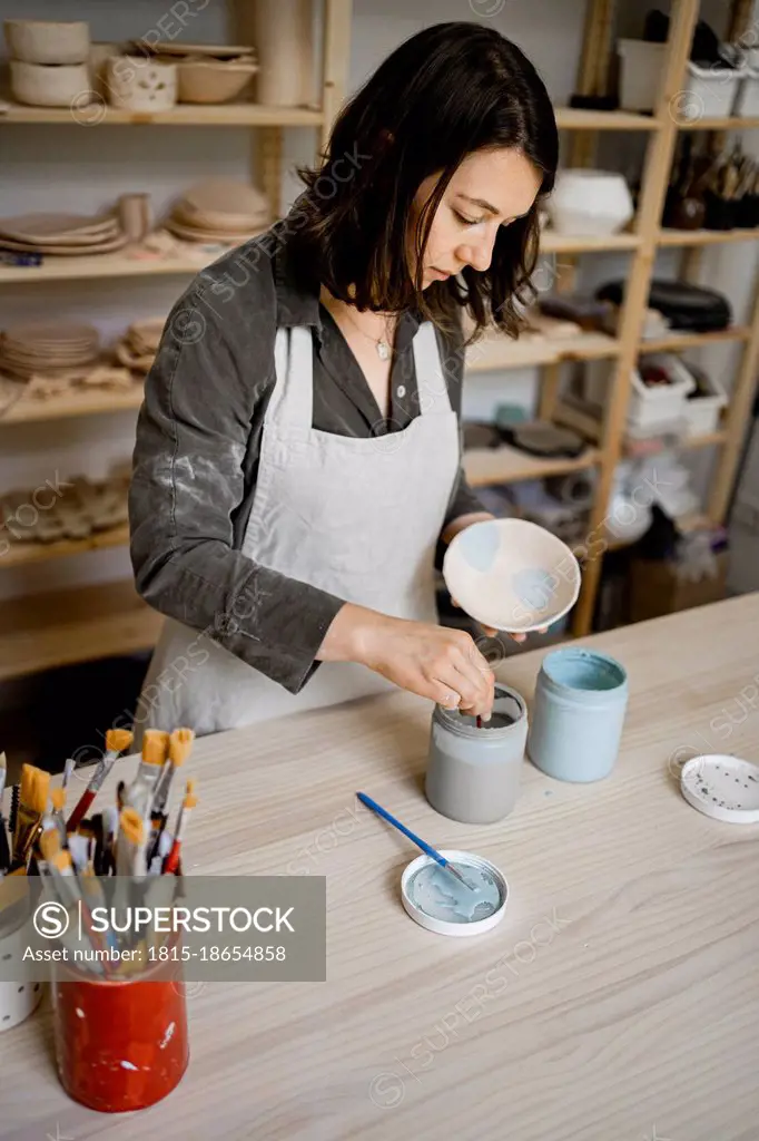 Female craftsperson painting bowl on workbench