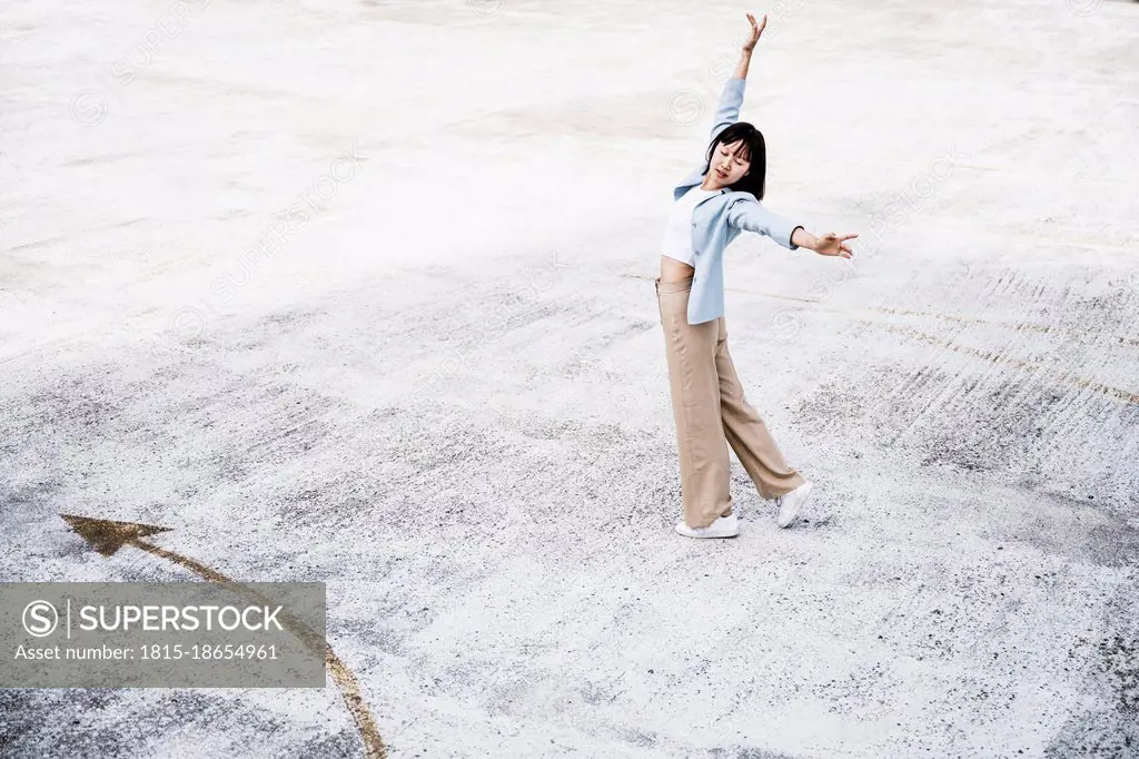 Teenage girl with arms outstretched dancing on parking garage rooftop