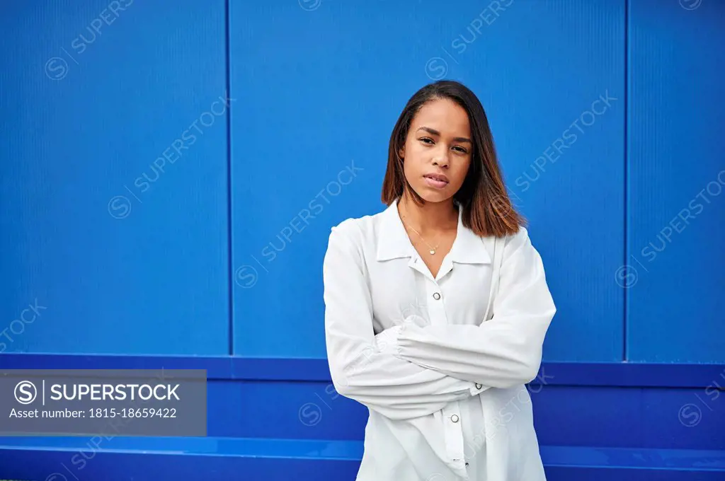Young woman with arms crossed standing in front of blue wall