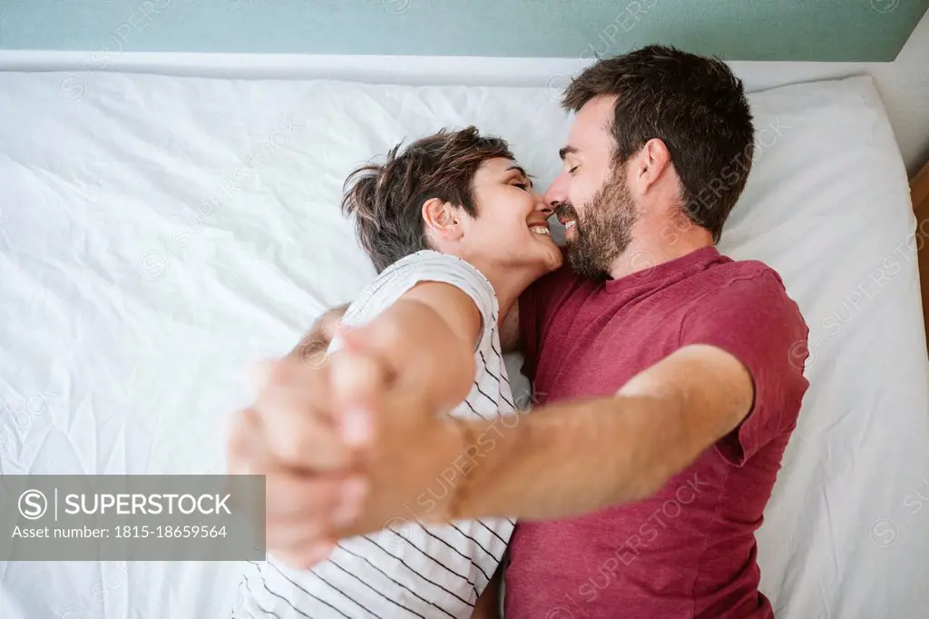 Affectionate couple with hands clasped lying on bed at home