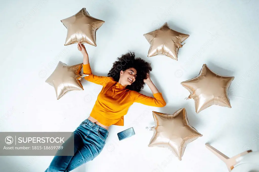 Smiling woman amidst star balloons lying on floor at home