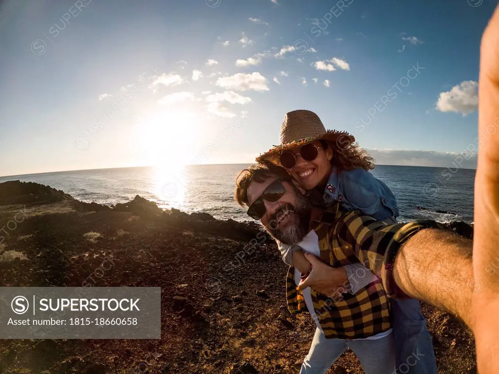 Happy mature man giving piggyback ride to woman while standing in front of sea