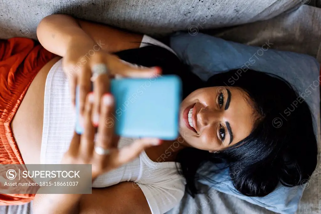 Smiling mid adult woman using smart phone while lying on sofa