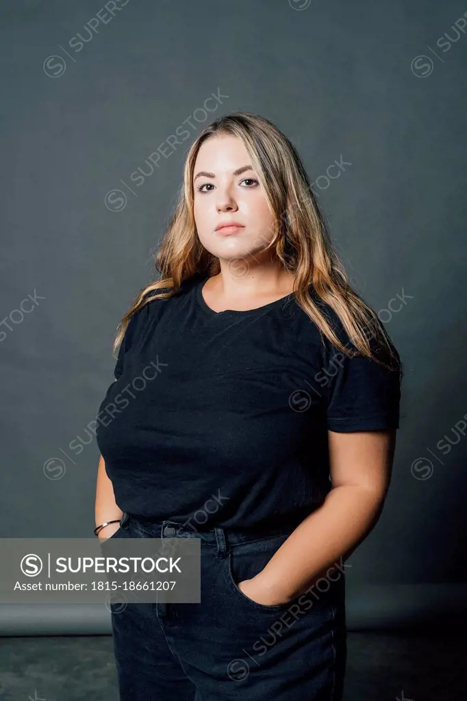 Confident voluptuous woman standing with hand in pockets at studio