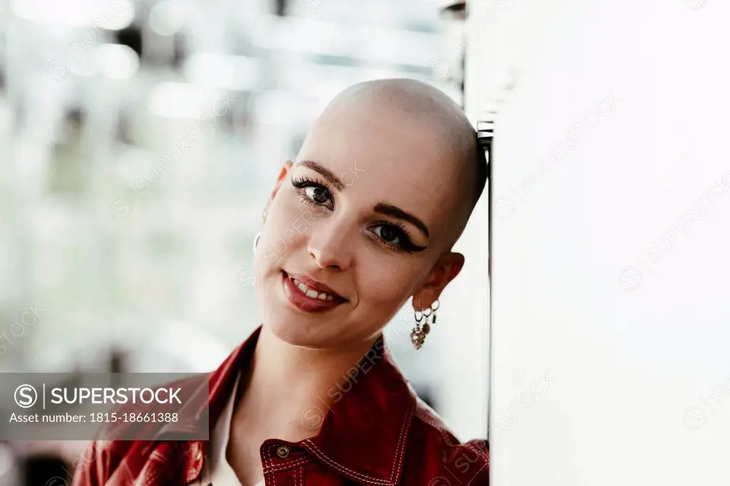 Smiling young bald woman leaning on wall