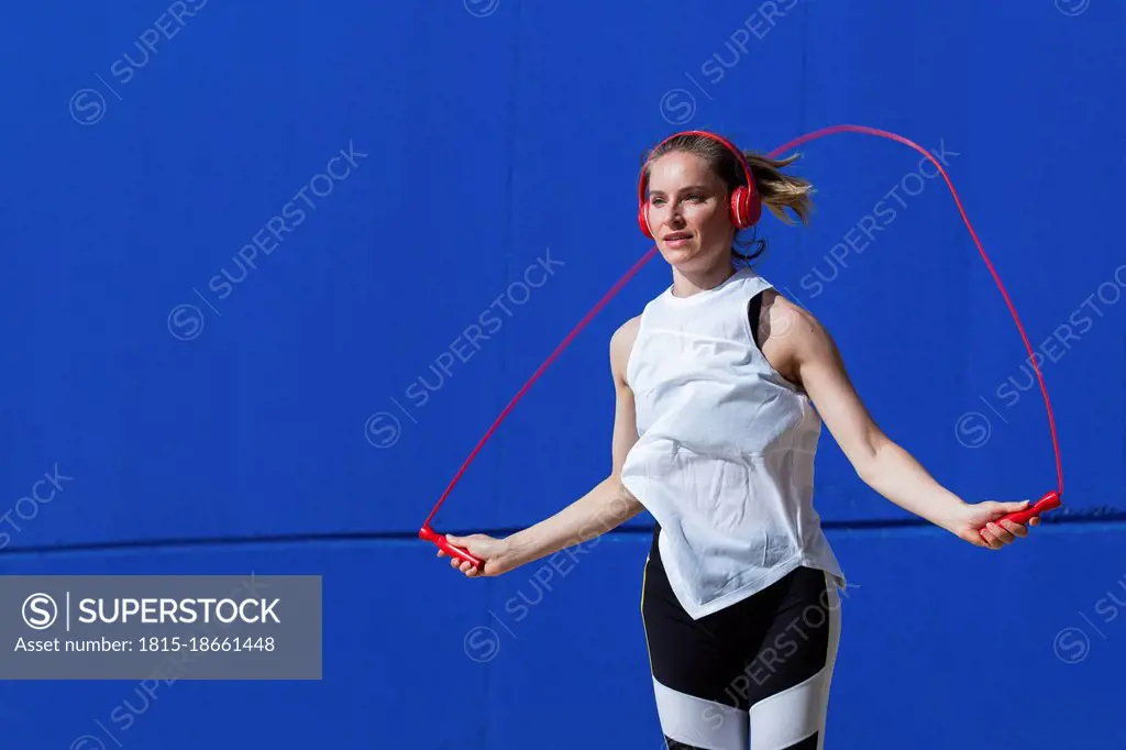 Female athlete jumping rope in front of blue wall