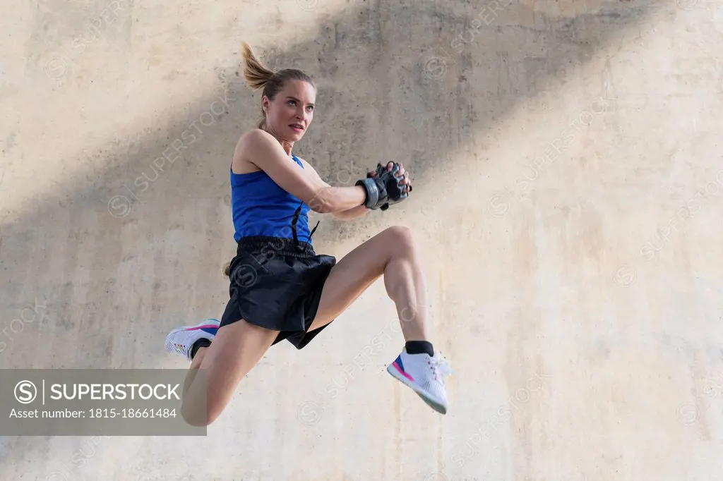 Determined female athlete jumping while exercising in front of wall