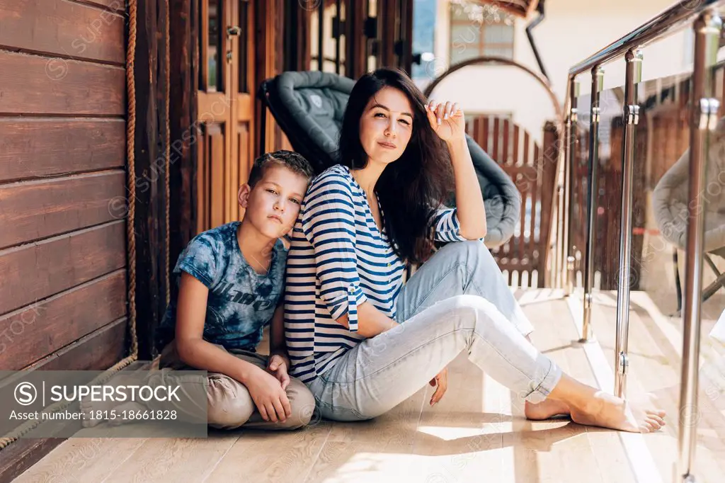 Son leaning on mother in balcony during sunny day