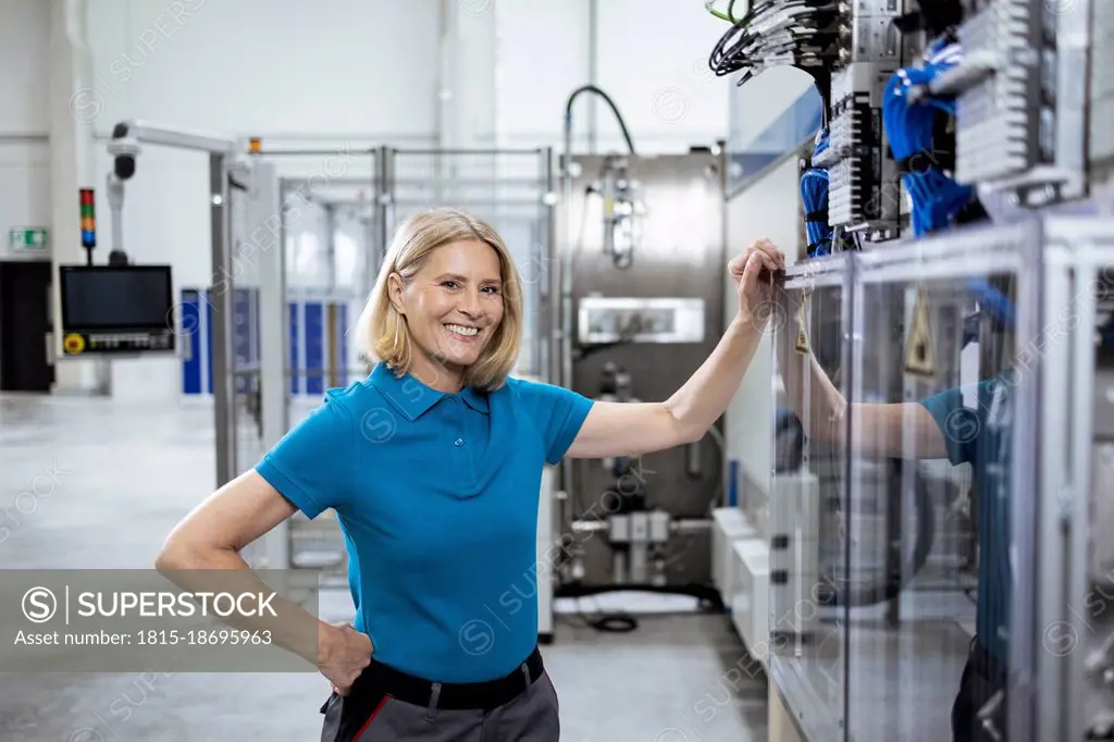 Smiling female professional with hand on hip standing by machinery in factory