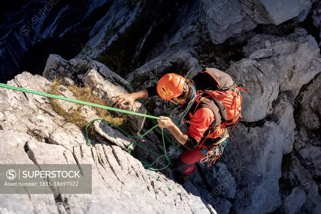 Determinant male Hiker moving down from mountain with rope on sunny day