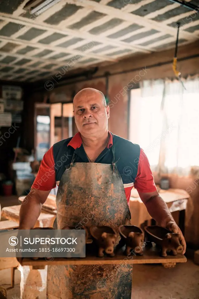 Potter holding plank of piggy banks in pottery