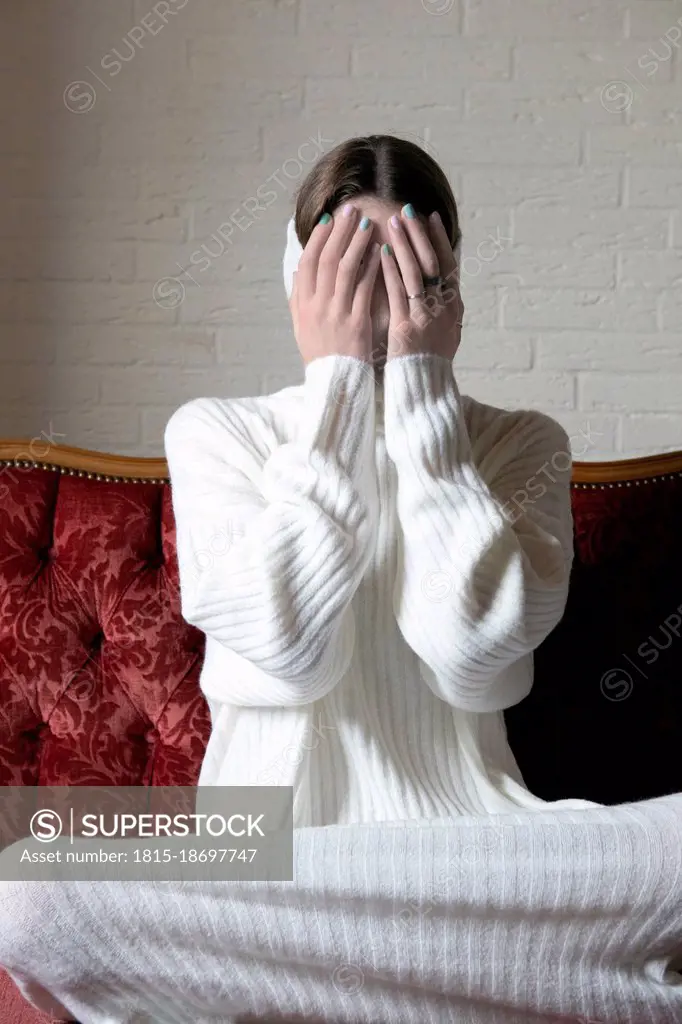 Teenage girl covering face with hands on sofa