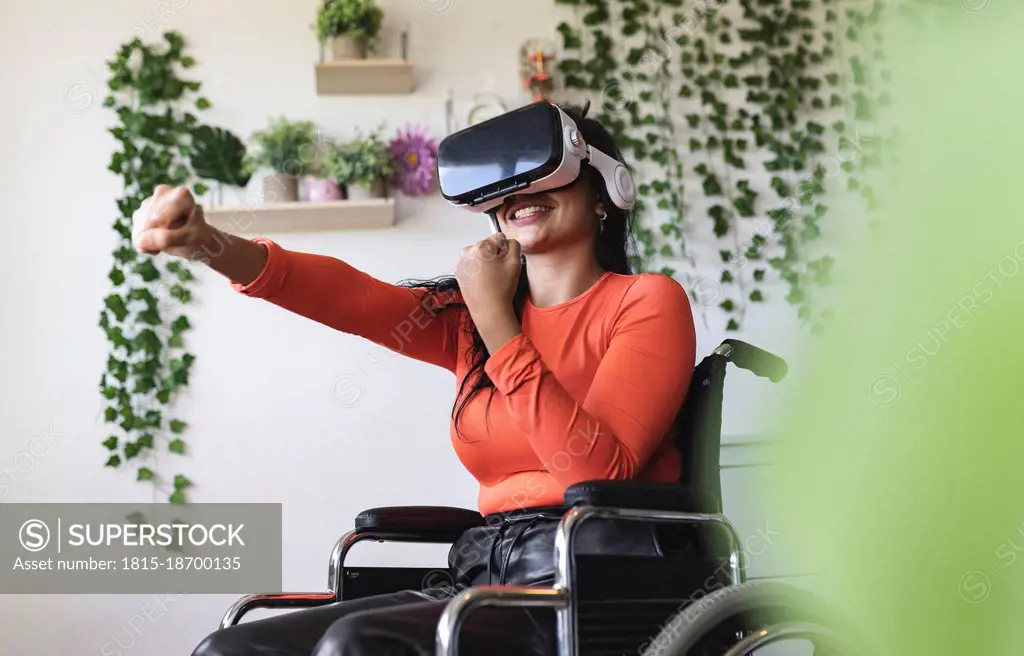 Smiling disabled woman wearing virtual reality headset gesturing at home