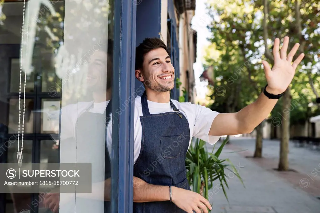 Smiling owner waving hand at cafe entrance