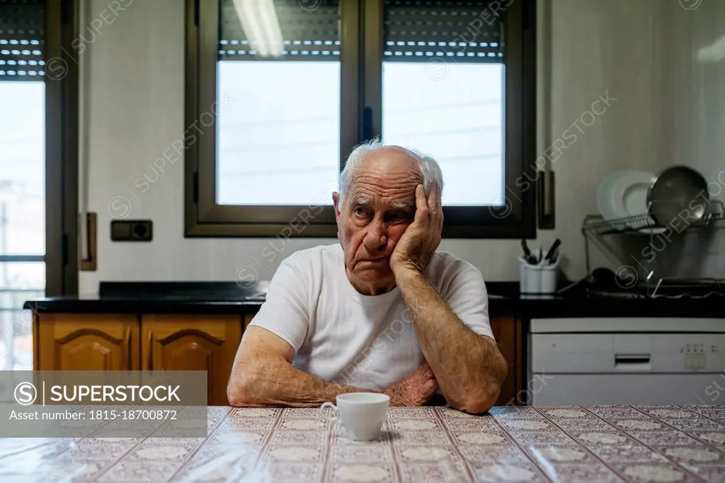 Sad man sitting at table in kitchen