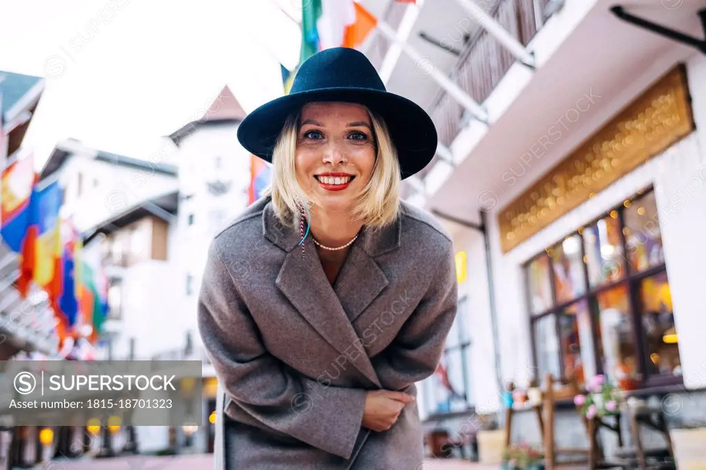 Smiling beautiful woman wearing hat and coat bending in city