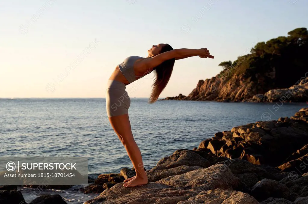 Flexible sportswoman practicing yoga on rock