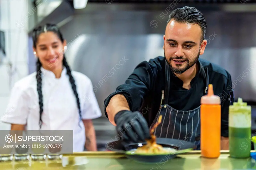 Chef decorating food with trainee in background