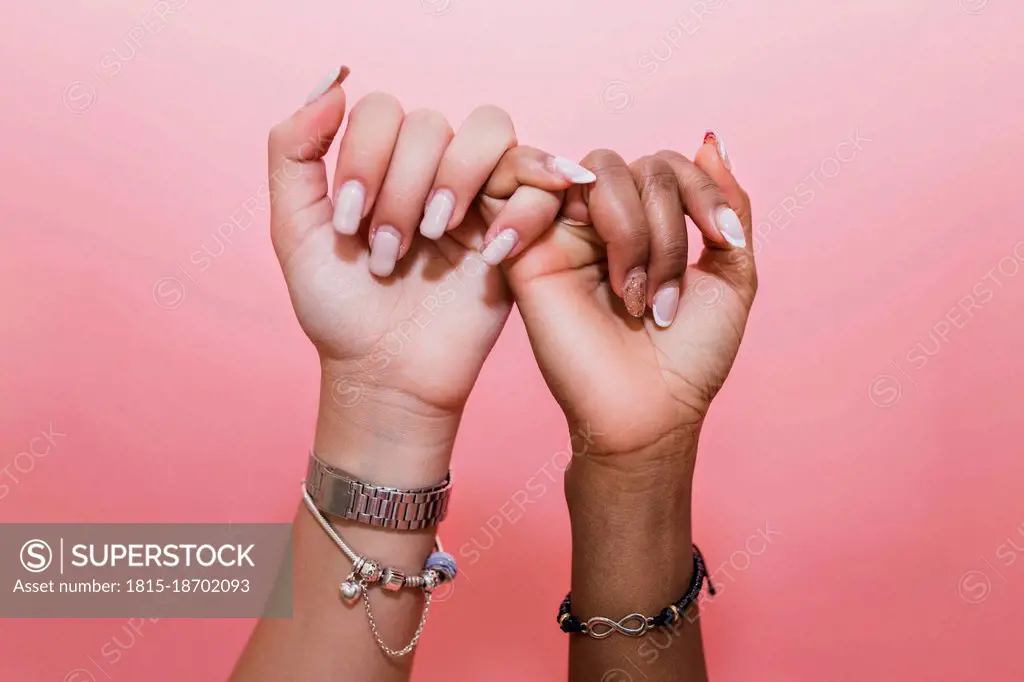 Lesbian couple making pinky promise against pink background