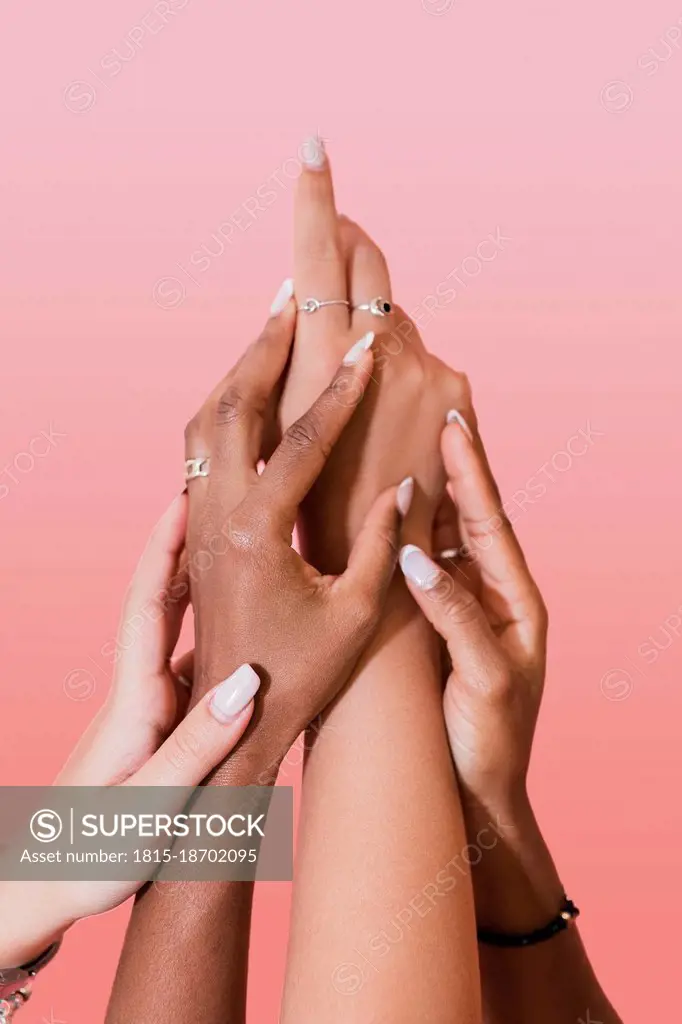 Multiracial lesbian women touching hands against pink background