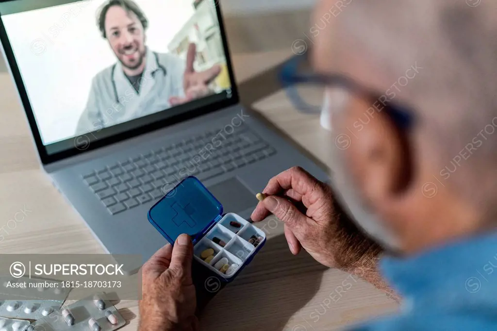 Man holding pill box on video call with doctor at home