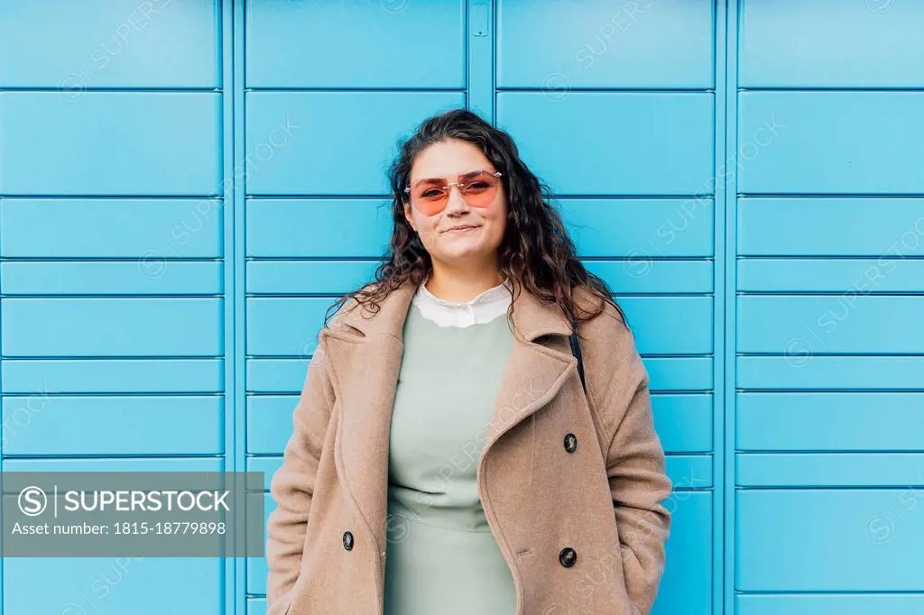 Smiling curvy woman wearing sunglasses in front of blue wall