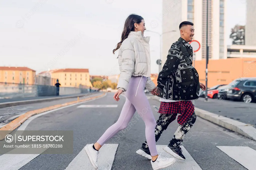 Young couple holding hands and crossing street in city