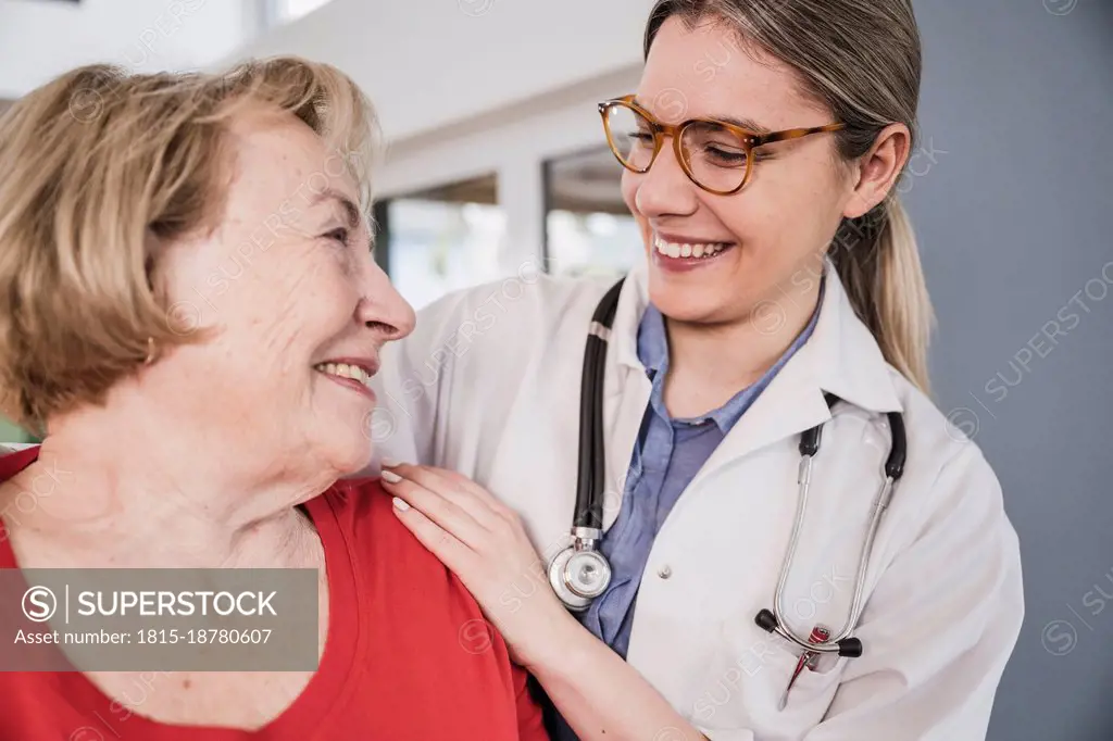 Smiling doctor with hand on senior patient's shoulder at home