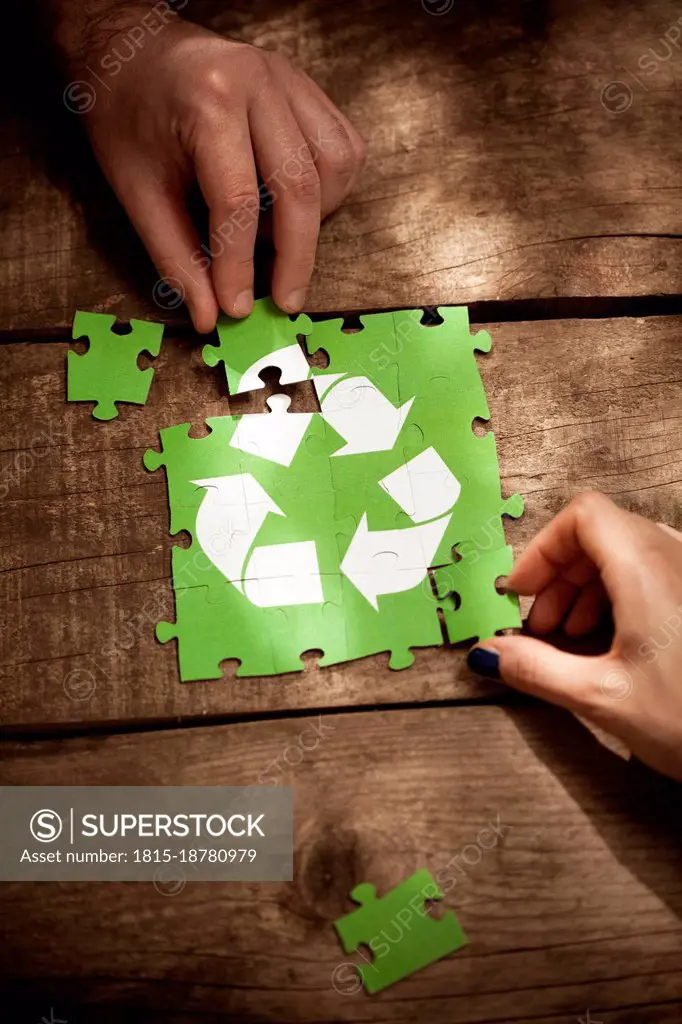 Friends joining recycling symbol jigsaw puzzle on table