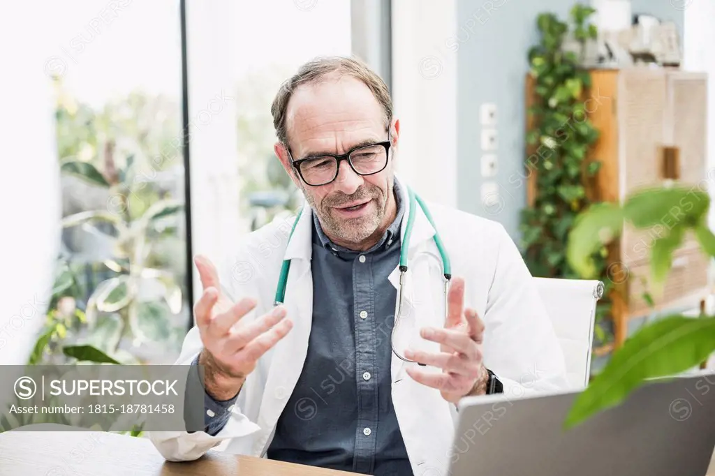 Doctor gesturing on video call through laptop at desk in hospital