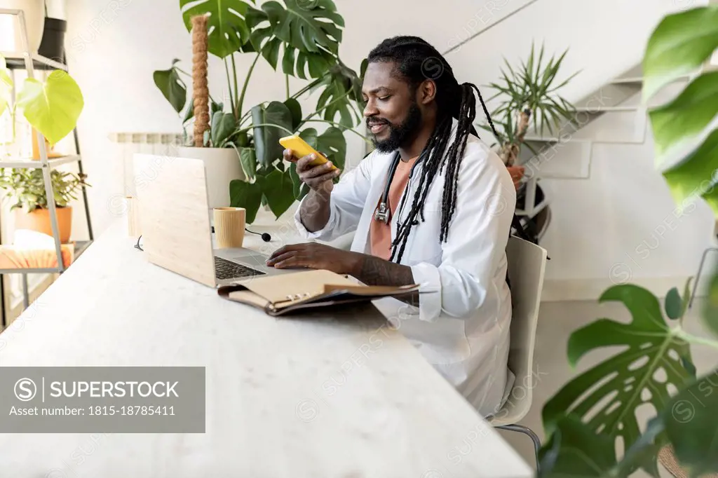 Doctor with laptop using smart phone at desk