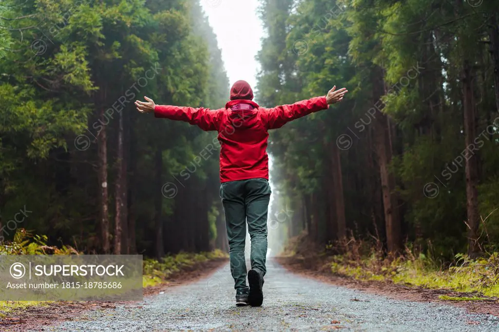 Man with arms outstretched walking on road at forest