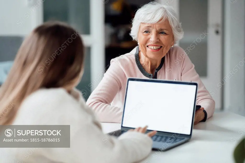 Woman looking at girl using laptop on table