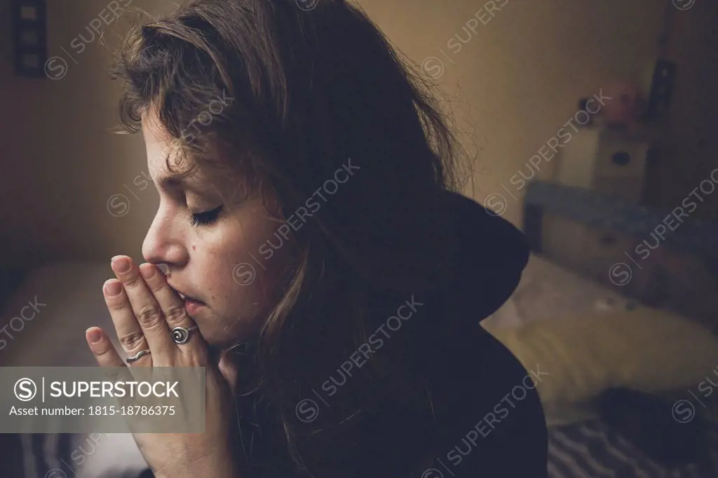 Woman with hands clasped praying at home