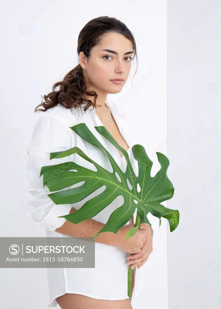 Beautiful woman with blank expression holding monstera leaf