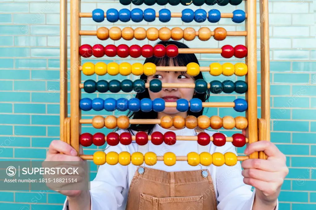 Young woman holding multi colored abacus in front of brick wall