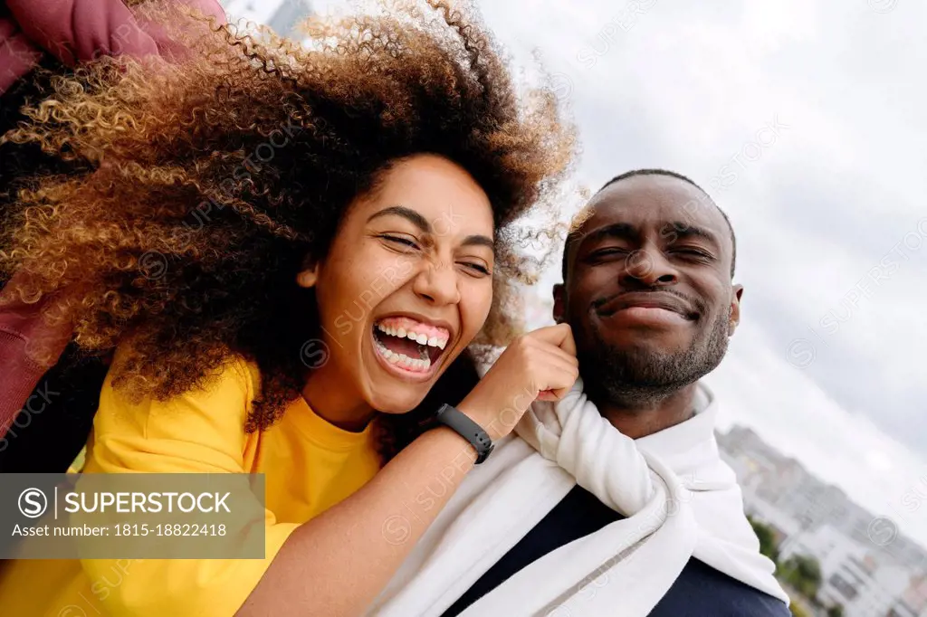 Happy young woman pulling cheek of friend outdoors