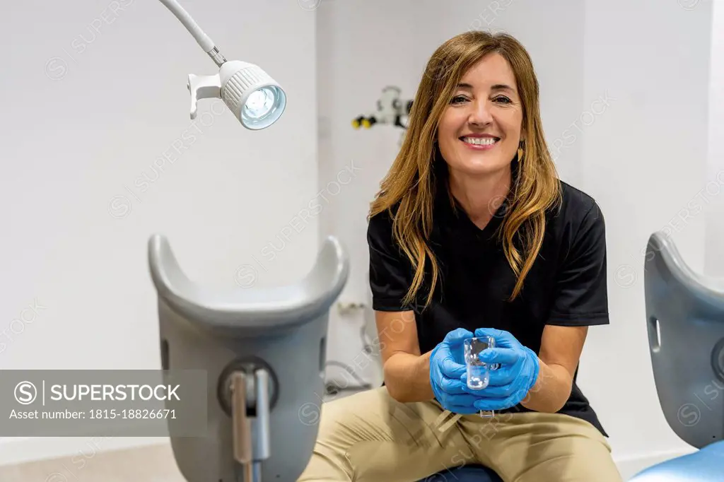 Smiling gynecologist wearing protective gloves sitting in clinic