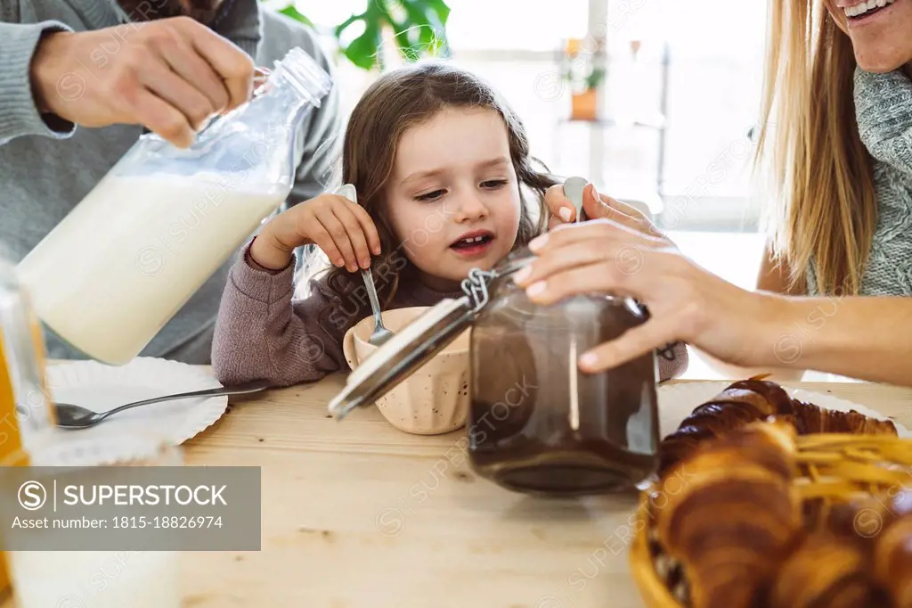 Cute girl having breakfast with parents at home