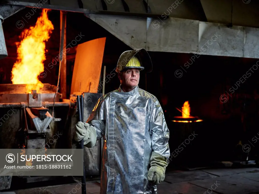 Contemplative blue-collar worker wearing helmet and protective suit in metal industry