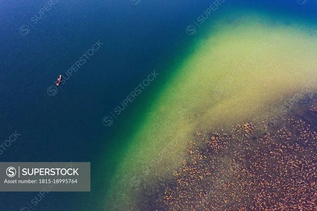 Drone view of fishing boat in front of reed belt stretching along shore of Irrsee lake in autumn