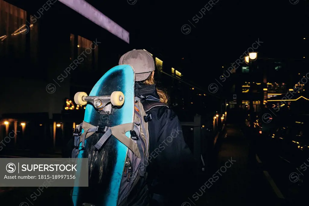 Man with backpack carrying skateboard at night