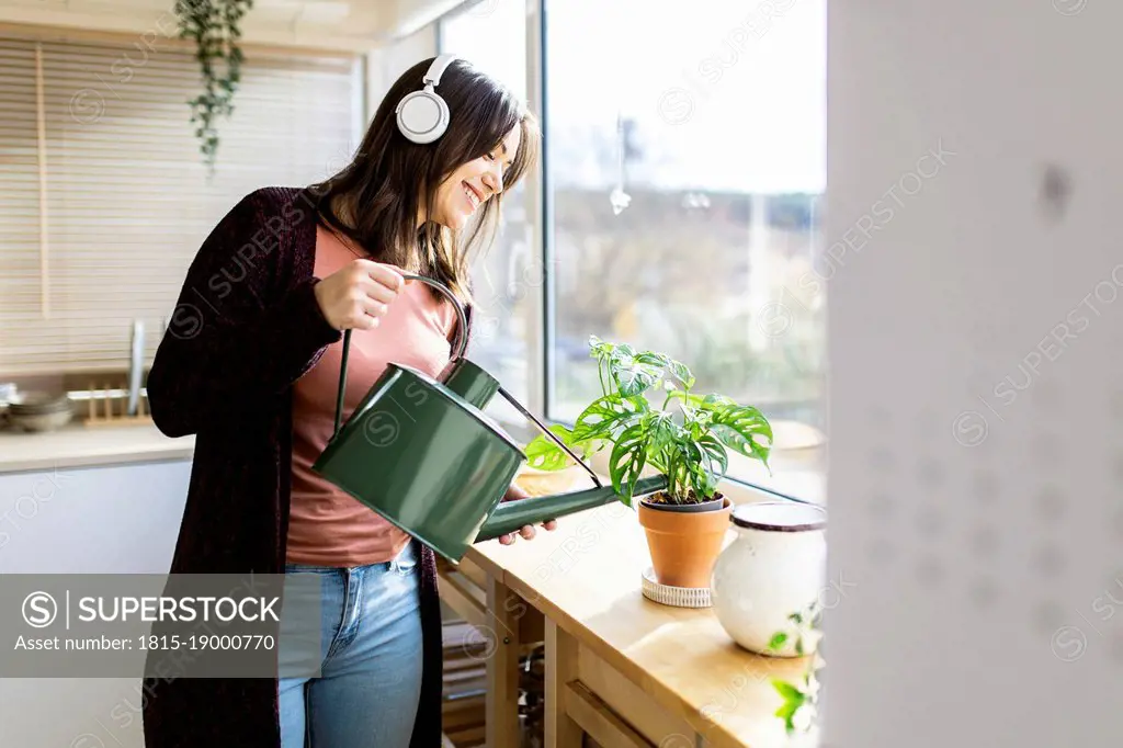 Woman listening music watering houseplant through can at home