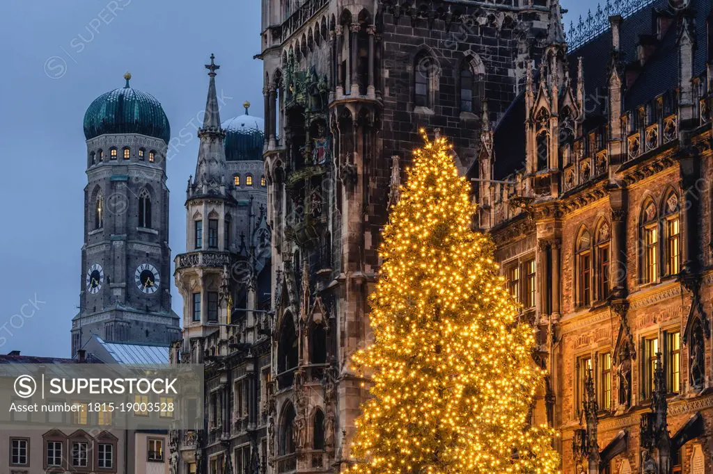 Germany, Bavaria, Munich, Christmas tree glowing on Marienplatz at dusk with Cathedral of Our Lady and town hall in background