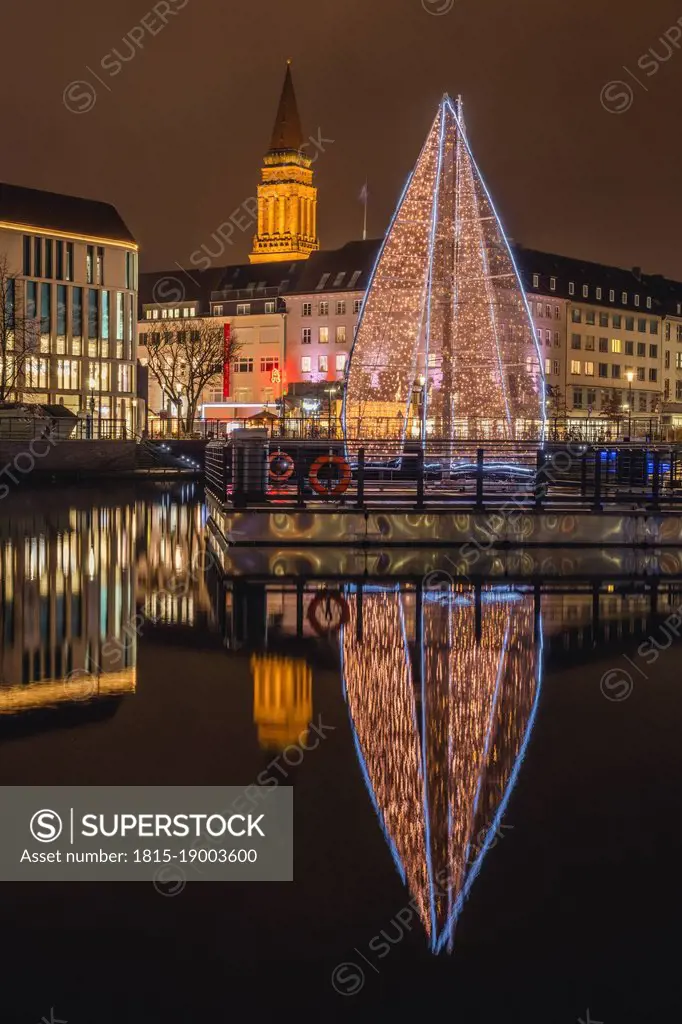 Germany, Schleswig-Holstein, Kiel, Large Christmas tree reflecting in city canal at night